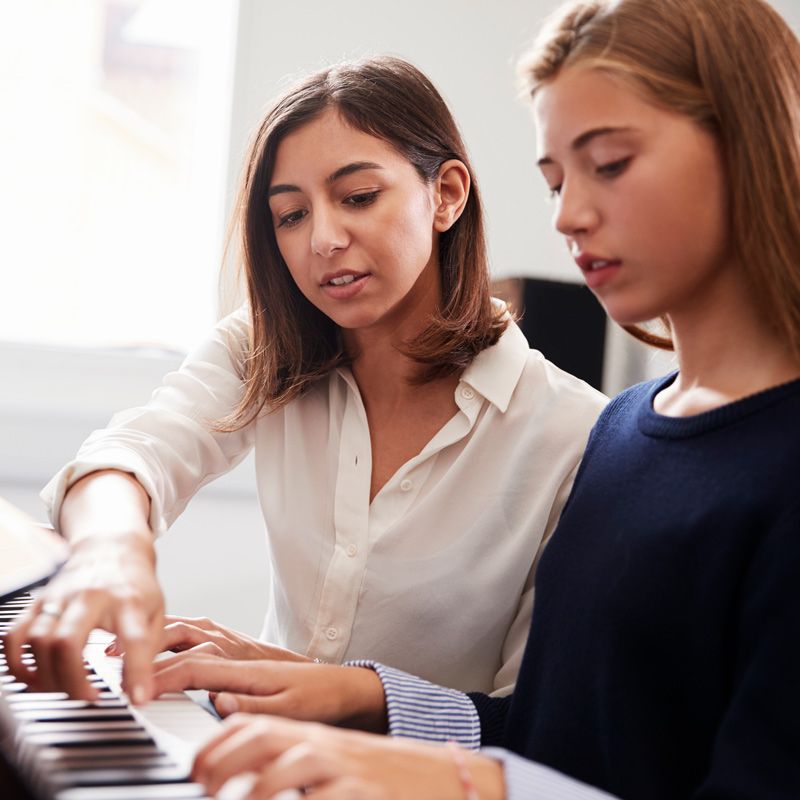 A piano teacher guiding a young student’s hands on the keyboard during a lesson